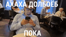 a man sitting at a table looking at his phone with a caption in russian that says " пока "