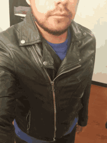 a man with a beard is wearing a black leather jacket and a blue shirt