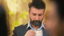 a man with a beard is sitting at a table drinking from a glass .