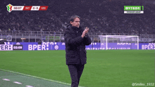 a man applauds on a soccer field in front of a banner for bper