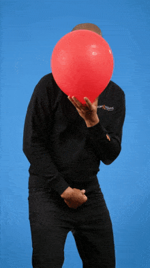 a man holding a red balloon in front of his face wearing a black sweatshirt with the word jesus on the sleeve