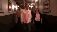 a group of people are walking down a hallway with a man in a pink shirt