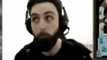 a man with a beard wearing headphones and a mask is looking at the camera .