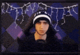 a man wearing a black and white beanie is sitting in front of a computer screen .