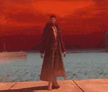 a man standing in front of a body of water with a red sky in the background
