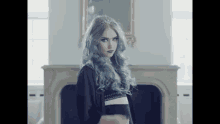 a woman with blue hair is standing in front of a fireplace and looking at the camera .