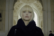 a woman with blonde hair and a scarf around her neck looks at the camera