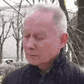 a close up of a man 's face with his eyes closed in front of trees