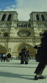 a woman stands in front of a large building with statues on it