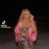 mariah carey is wearing a pink robe and a sequined dress while holding a glass of wine .