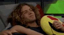 a young man with curly hair is laying on a couch holding a yellow pillow in the shape of a heart .