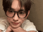 a young man wearing glasses and a white shirt is laying down with his hands on his chin .