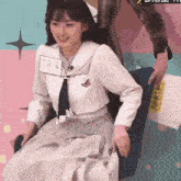 a girl in a school uniform is sitting in a chair with a man holding her arm