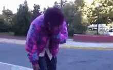 a person wearing a purple and blue tie dye jacket is standing on the sidewalk .