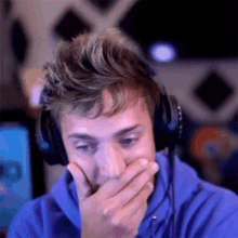 a man wearing headphones is covering his mouth with his hand while looking at a computer screen .