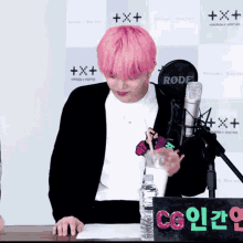 a person with pink hair is standing in front of a rode microphone