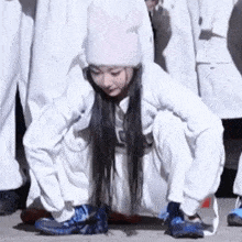 a woman in a white hat and white pants is squatting on the ground .