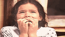 a little girl is biting her nails and looking at the camera