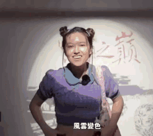 a woman in a purple shirt stands in front of a wall with chinese characters on it
