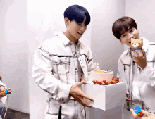 two young men holding a stuffed animal and a cake
