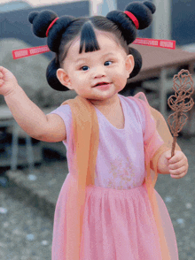 a little girl wearing a pink dress holds a stick