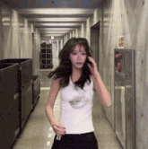 a woman in a white tank top is walking down a hallway