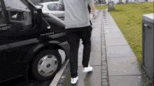 a man is walking down a sidewalk next to a black transit van