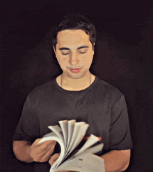 a man in a black shirt is reading a book with a red bookmark