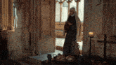 a nun stands in front of a table with bread and a candle in front of a window ..