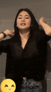 a woman in a black shirt and blue jeans has a yellow smiley face on her face
