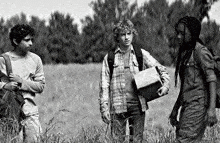 a black and white photo of three people standing in a field . one of the people is holding a box .