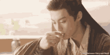 a man with long hair is drinking from a glass with the words love between fairy and devil written above him