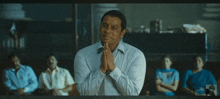 a man in a white shirt is praying with his hands folded in front of a group of people