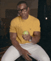 a man wearing glasses and a yellow prada shirt is holding an apple