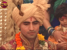 a man wearing a turban with a peacock feather on top of it is being helped by a woman
