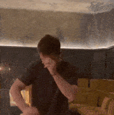 a man in a black shirt is covering his face in a living room
