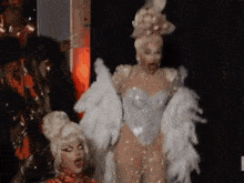 a couple of drag queens are standing next to each other on a stage with feathers in their hair .