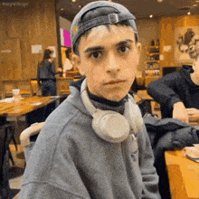 a young man wearing headphones and a hat is sitting in a restaurant .