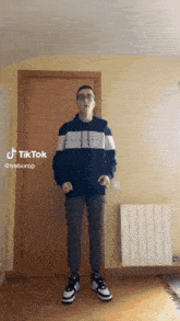 a young man is standing in front of a door in a room with a radiator and a tiktok sticker .