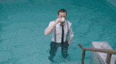 a man in a suit and tie is sitting on a bench in a bathroom holding his shoes .