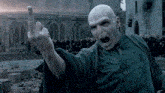 a bald man in a green robe is giving the middle finger to a crowd of people .