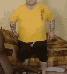 a man in a yellow shirt and black shorts is standing on a chair