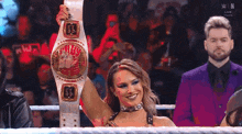 a woman is holding a wrestling championship belt in a ring in front of a crowd .