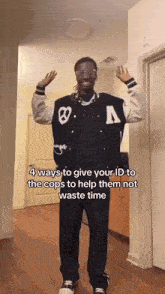 a man wearing a varsity jacket and glasses is standing in a hallway with his hands in the air .