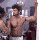 a shirtless man standing next to a woman in a room