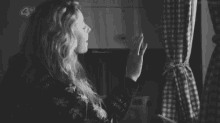 a black and white photo of a woman holding a plaid curtain .