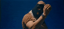 a person wearing a ski mask and sunglasses holds a watch