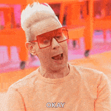 a man wearing sunglasses and an orange shirt is making a funny face and saying okay .