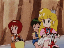 a girl with blonde hair is riding a bike next to a boy and a girl with red hair