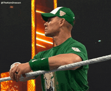 a man in a green shirt stands in a wrestling ring with his hands on the ropes